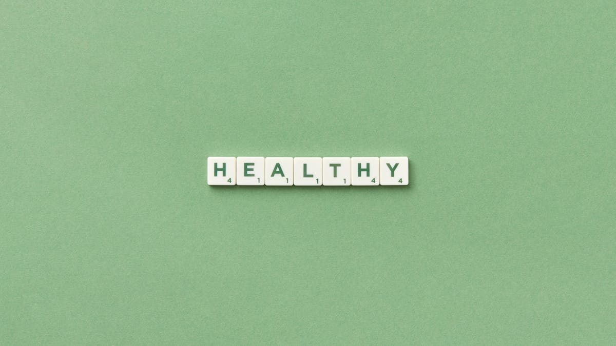Scrabble tiles spelling the word 'healthy' on a light green background, top view.